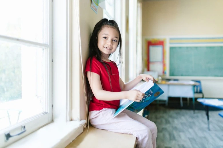 Anak tersenyum ceria saat membaca buku, salah satu langkah cara mengembalikan semangat belajar anak setelah libur.
