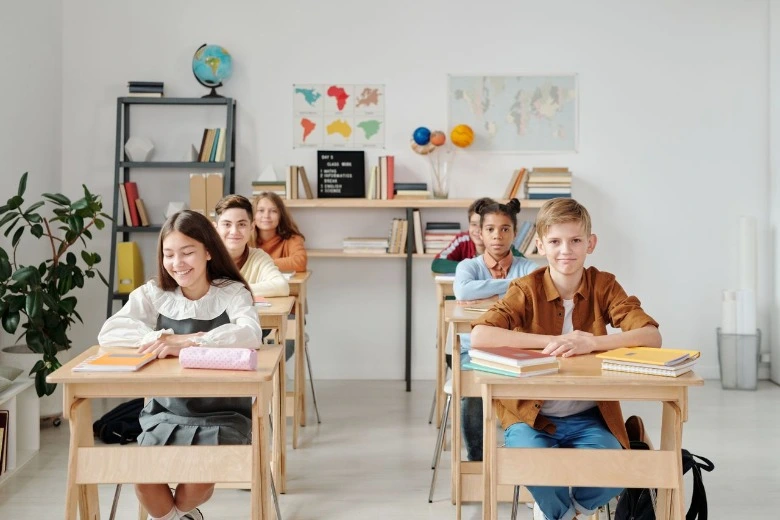 Sekelompok murid mengangkat tangan dan berinteraksi di ruang kelas yang ceria saat masa adaptasi anak masuk sd.